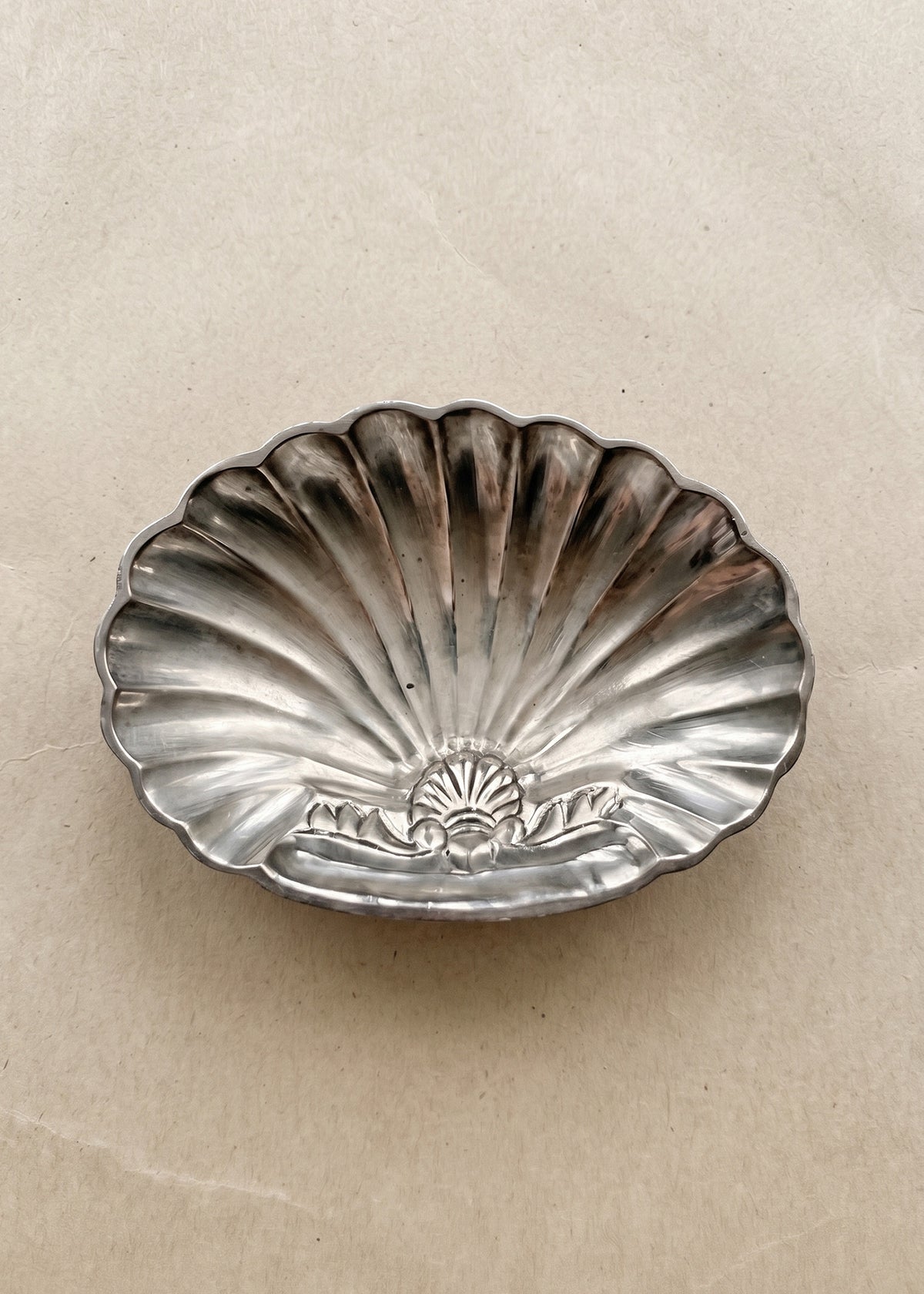 Vintage silver-toned shell-shaped soap dish with natural patina on warm neutral background